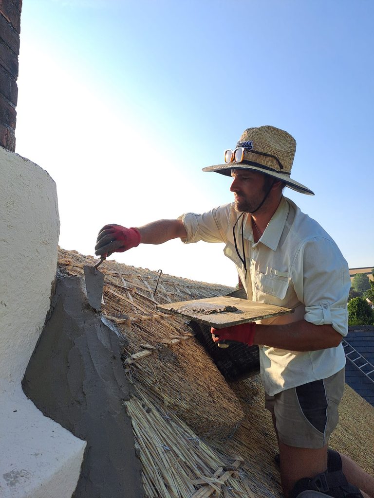 Luke Robinson Master Thatcher installing chimney flashing on thatched roof